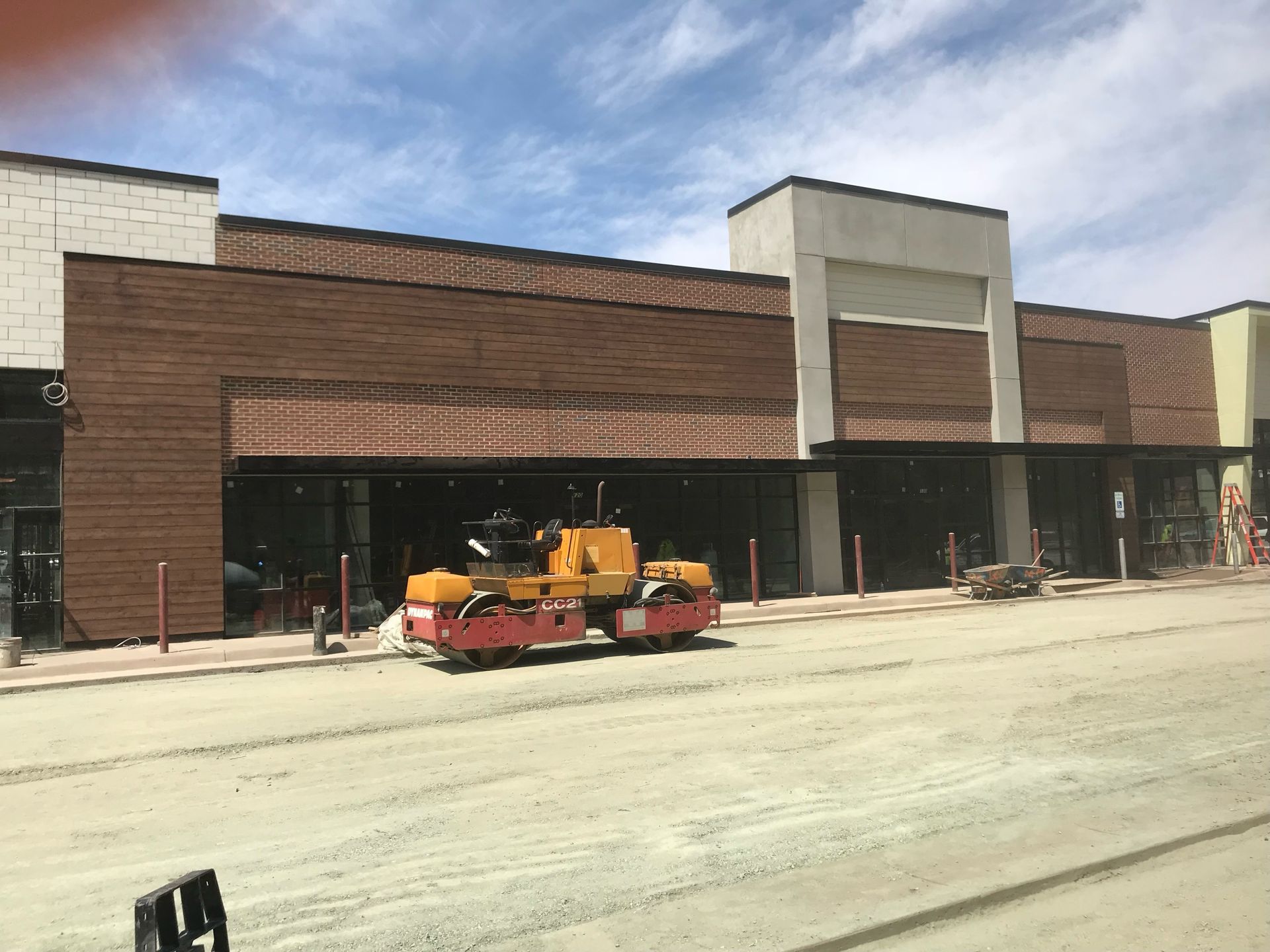 Brick storefront under construction with a yellow utility vehicle in front and concrete sidewalk work underway