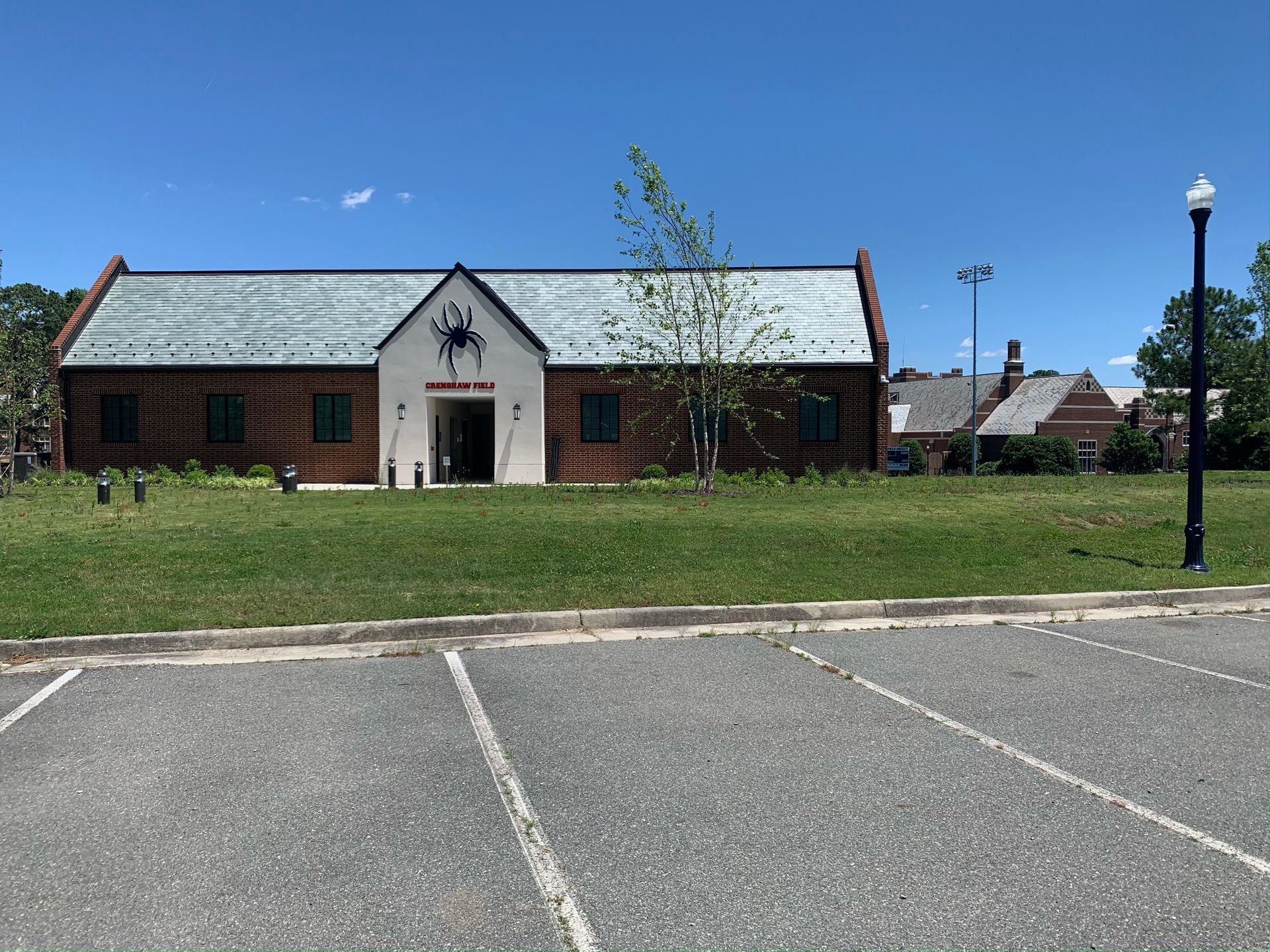 Small brick building with a white entrance gable, grassy lawn, and parking lot under a clear blue sky.