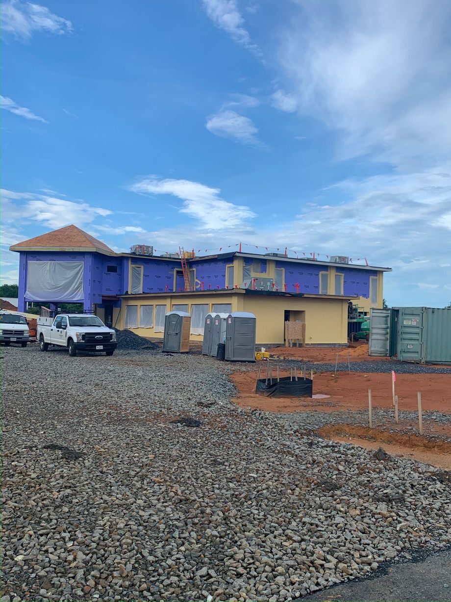 Partially constructed blue building with gravel foreground, parked truck, and cloudy sky
