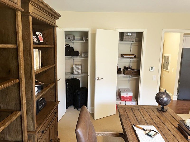 Home office with wooden bookshelf, desk, open closets, and doorway to hallway