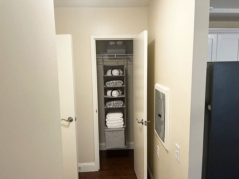 Narrow hallway with an open linen closet stacked with towels and shelves, white walls and dark wood floor