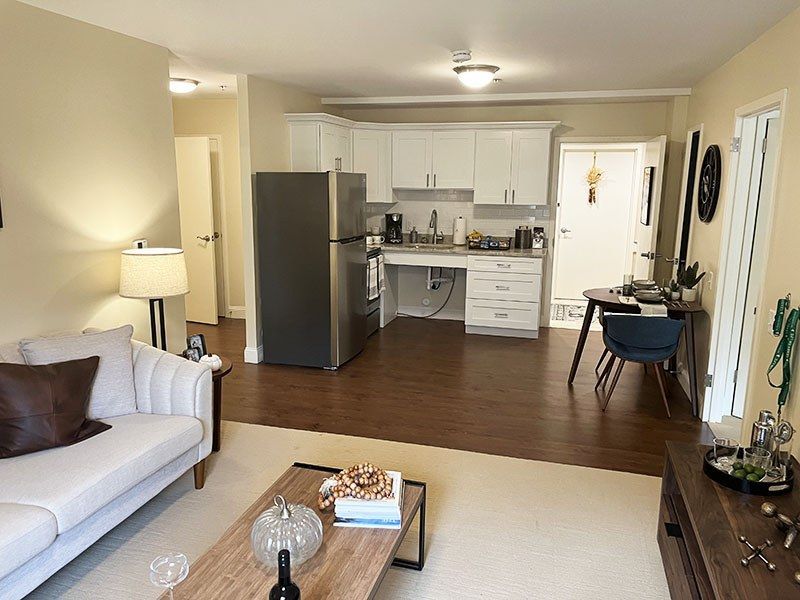 Open-plan living room and kitchen with white sofa, dark wood floors, and stainless-steel refrigerator