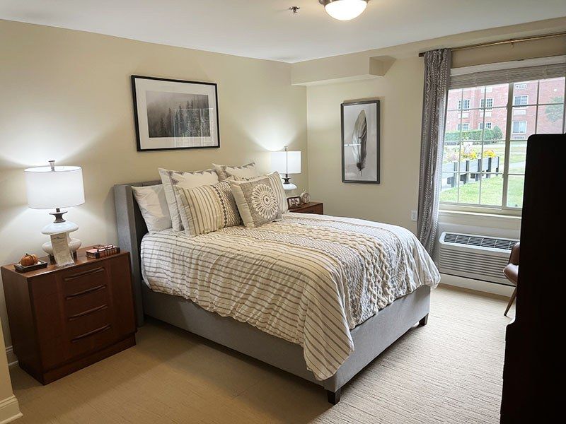 Bright bedroom with a neatly made bed, nightstands, lamps, and a window with curtains.