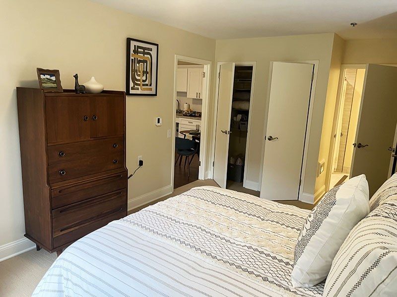 Bedroom with white bedspread, wood dresser, mirrored closet doors, and an open doorway to a bathroom.