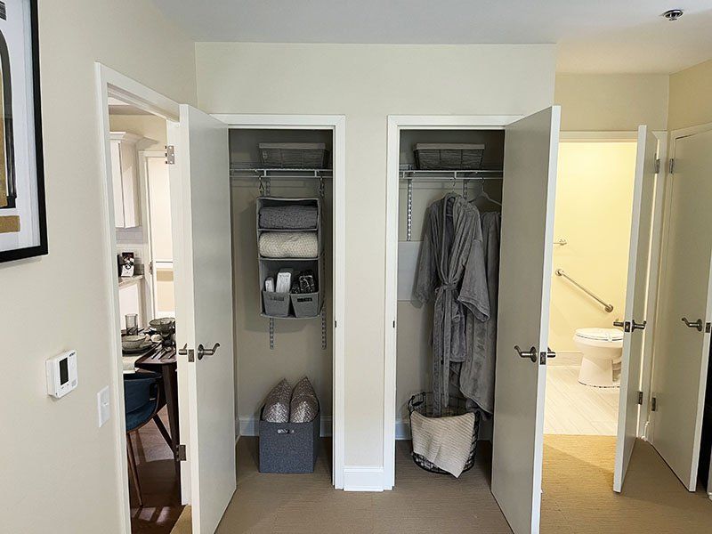 Open closet with shelves and hanging clothes between two bathroom doors in a bright hallway