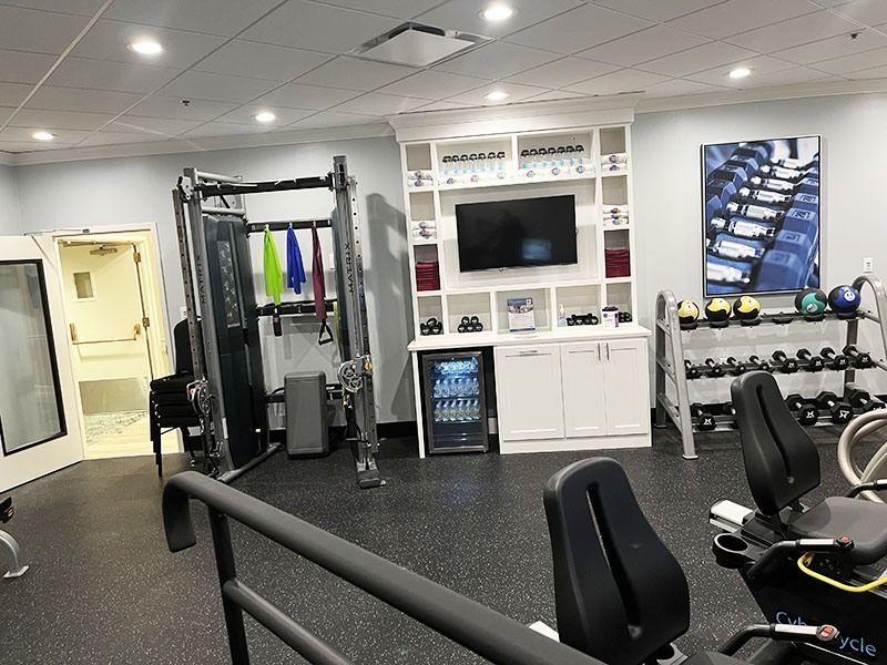 Gym interior with cable machine, white cabinets, TV, dumbbells, and black exercise equipment