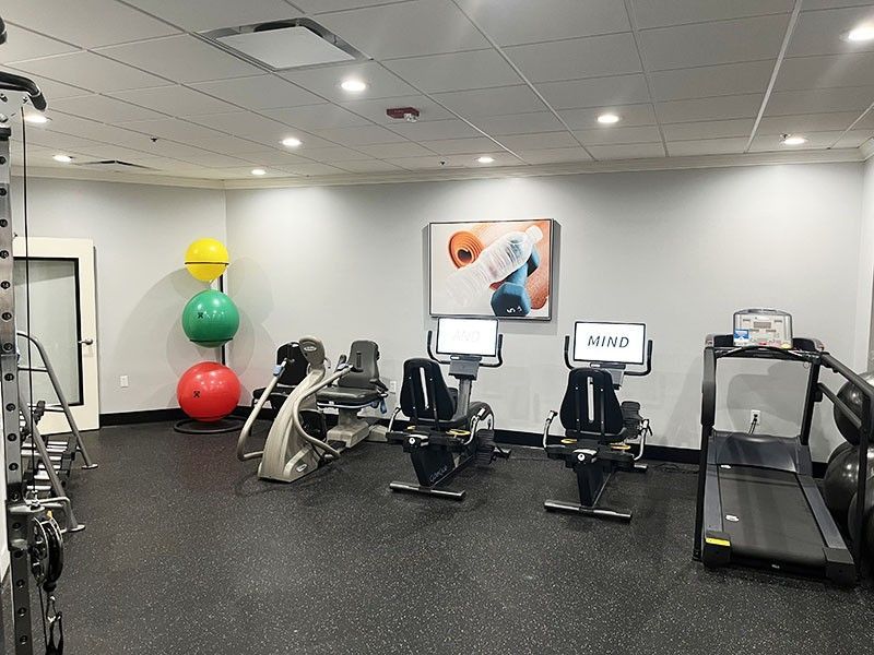 Small gym room with treadmills, exercise bikes, and colorful stability balls against white walls.