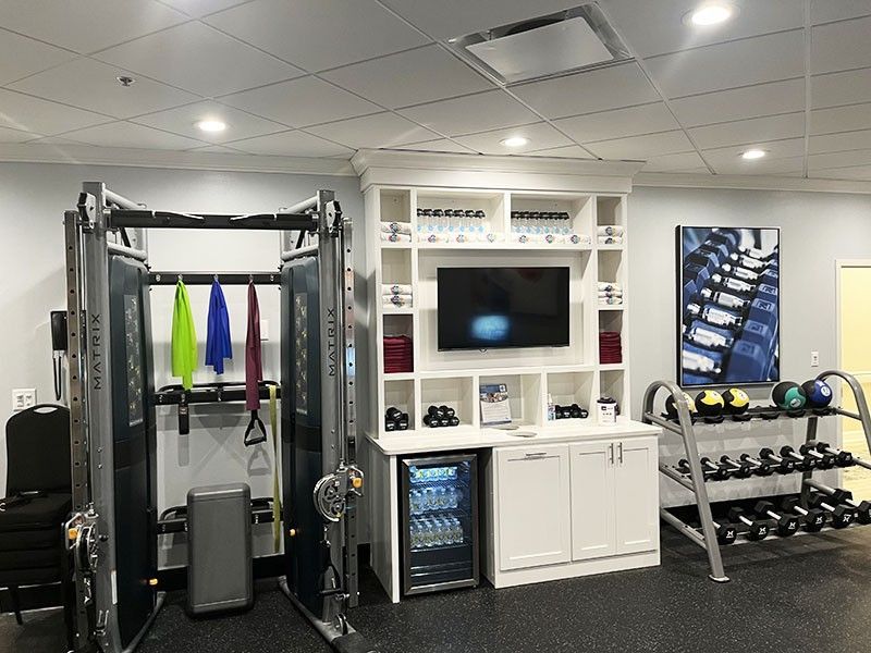 Modern gym with cable machine, dumbbells, TV, and cabinets in a bright white room