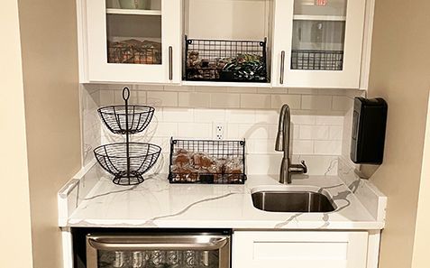 Compact white kitchen counter with sink, wire basket decor, glass cabinets, and stainless stove below