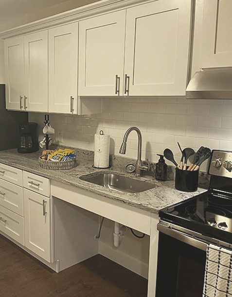 White kitchen with granite countertops, stainless sink, upper cabinets, stove, and countertop appliances