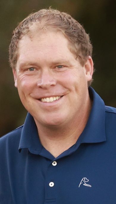 Smiling man in a blue polo shirt against a blurred outdoor background