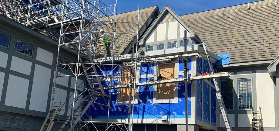 Blue scaffolding around a house under repair, with a ladder and roof work in progress