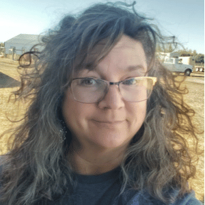 A woman wearing glasses and a blue shirt is smiling for the camera.