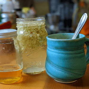 jar of honey, steeping elderflowers, a blue mug with a spoon inside