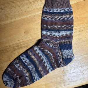 Brown, blue, and cream patterned knitted sock on a wooden surface.