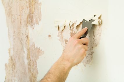 A person is peeling off wallpaper from a wall with a spatula.