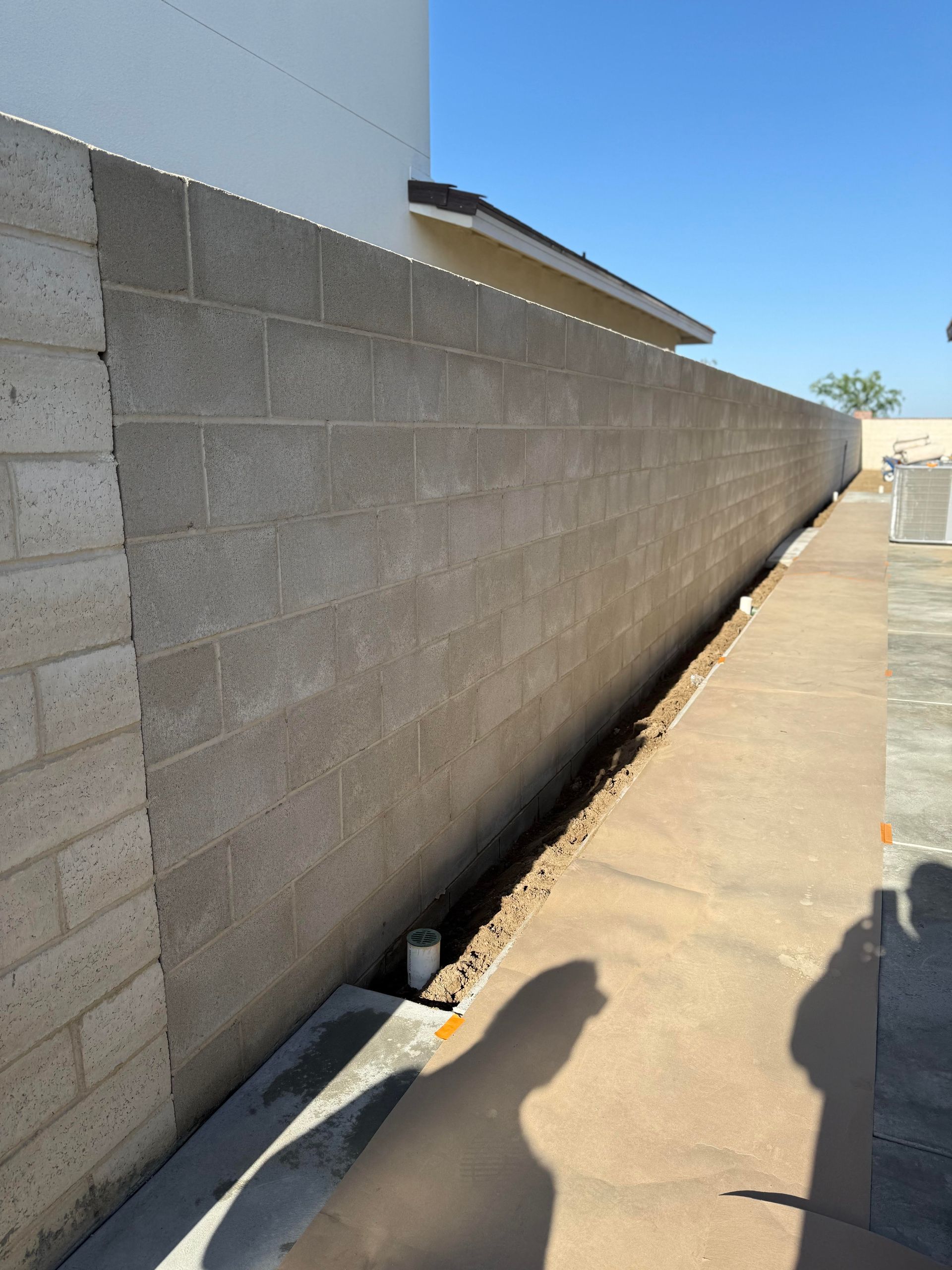 A brick wall along a sidewalk with a house in the background