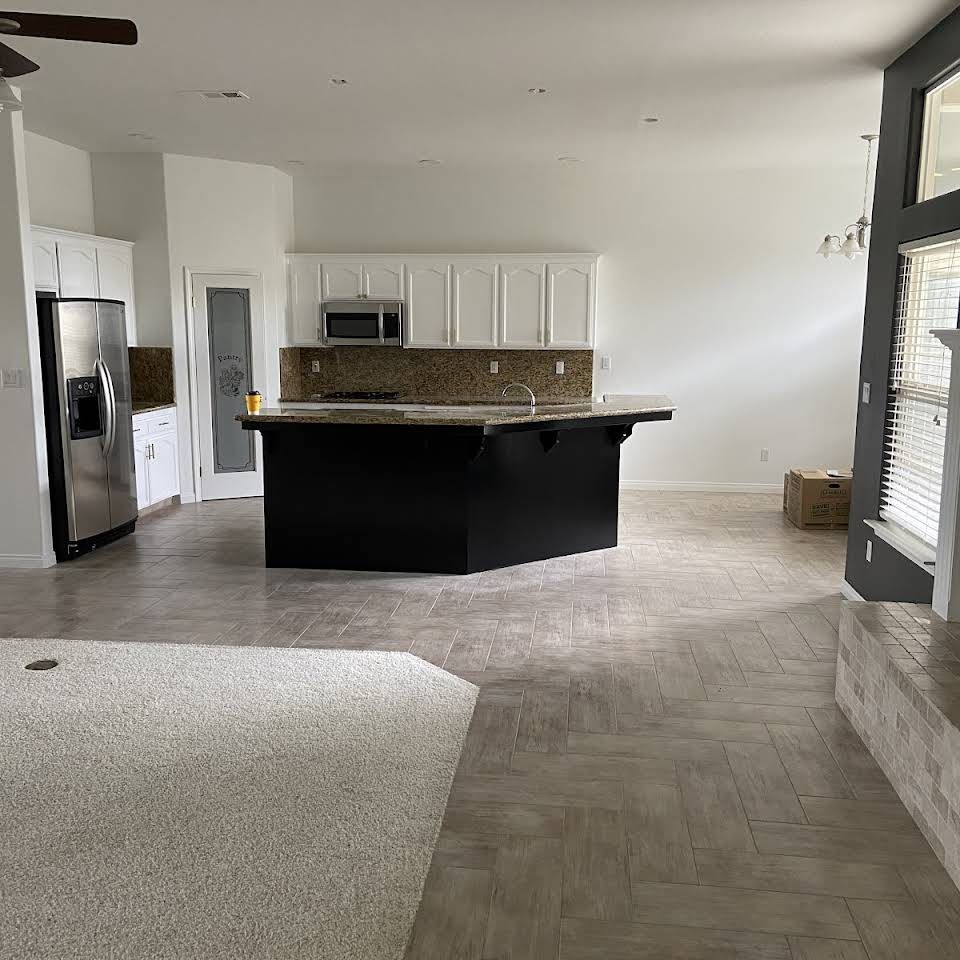 A kitchen with a black island , white cabinets , stainless steel appliances and a ceiling fan.
