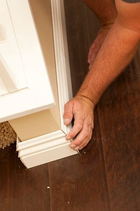 A man is installing a white molding on a wooden floor.