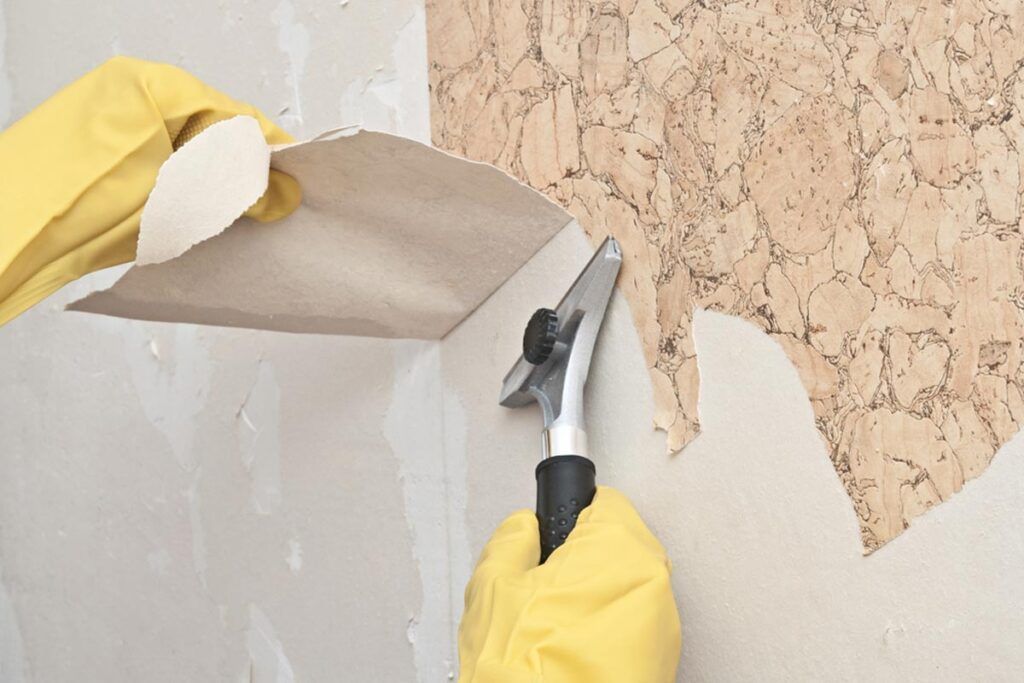 A person is removing wallpaper from a wall with a spatula.