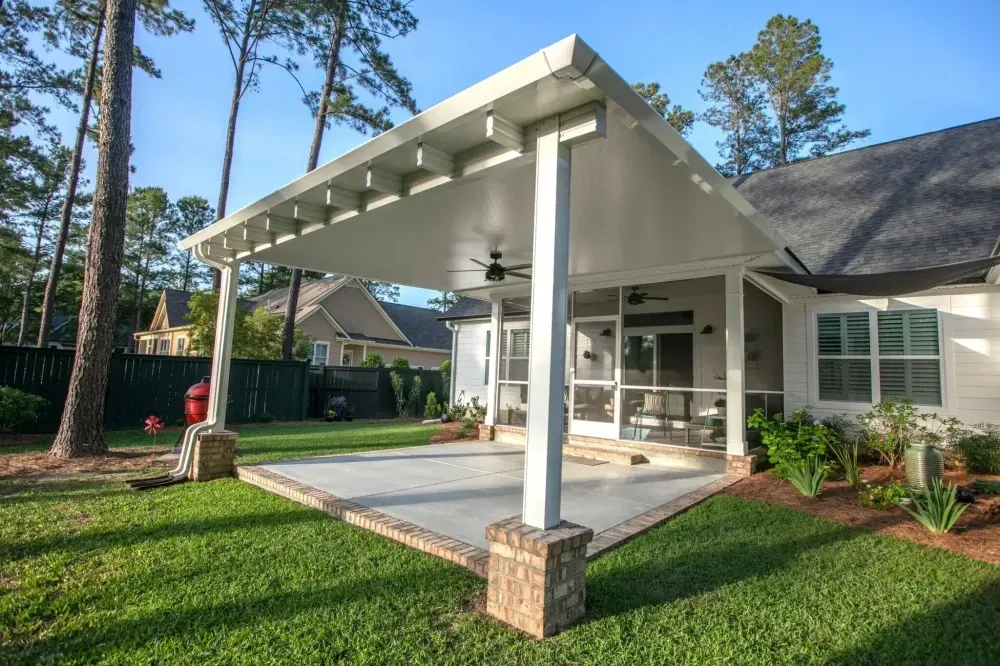 Covered backyard patio with white beams, stone columns, and a grassy lawn beside a house