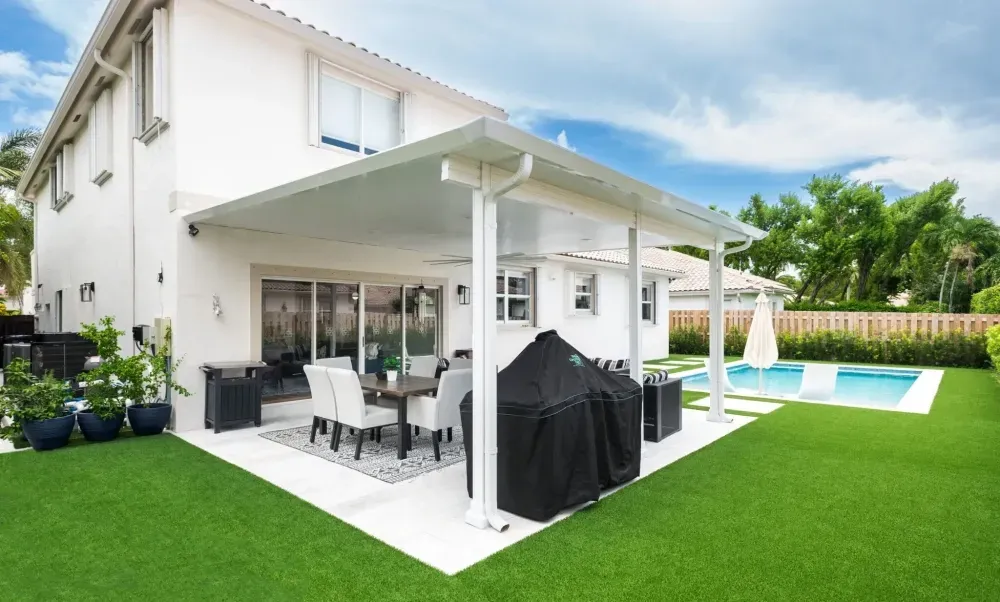 Modern house patio with outdoor dining set, grill, and swimming pool beside a bright green lawn