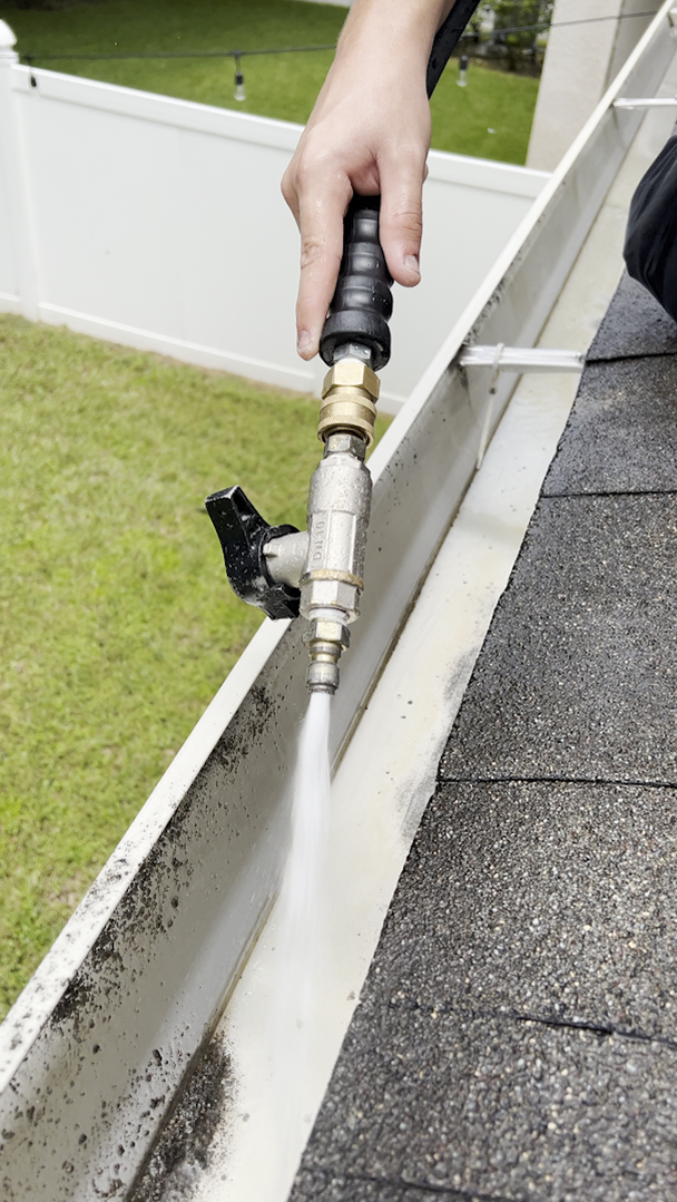 A person cleaning a gutter with a power washer on a rooftop, outdoors.