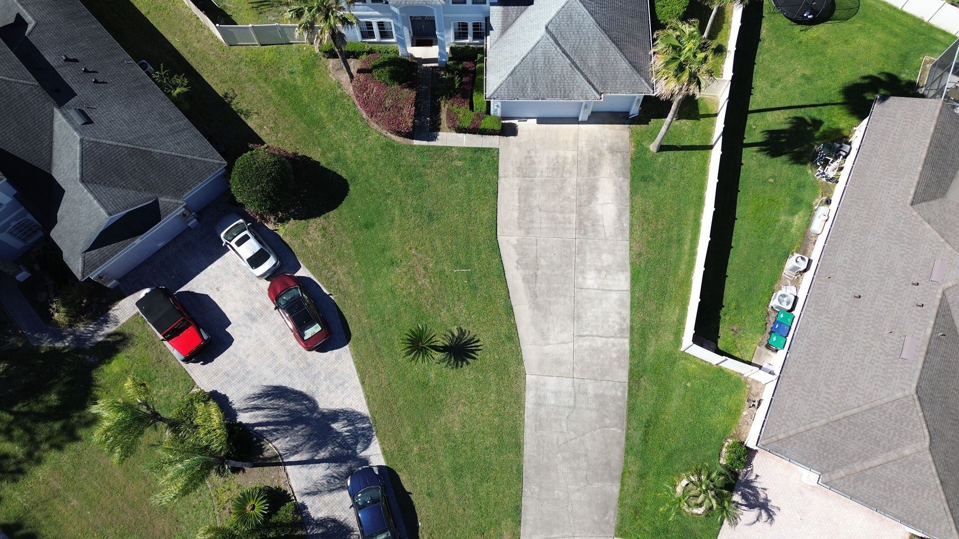 Aerial view of suburban houses with driveways, cars parked on driveways and lush green lawns.