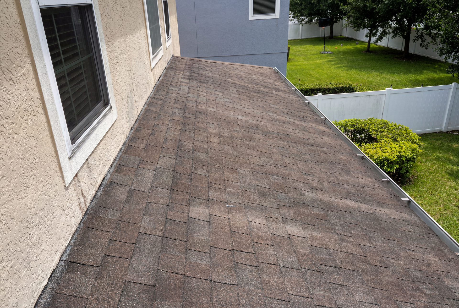 Close-up of a brown shingle roof on a beige house, with a grassy lawn in the background.