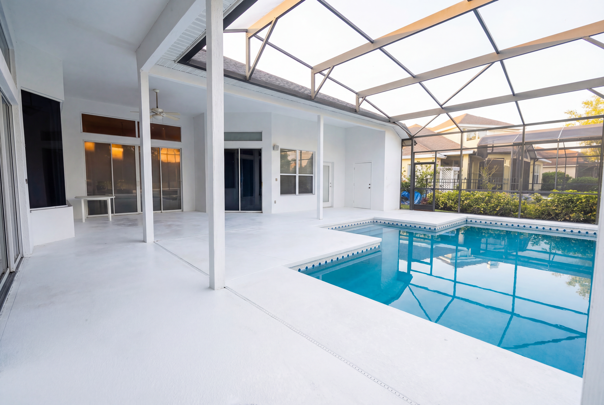 A white-walled patio with a pool enclosed by a screen. Blue pool water contrasts with the white.