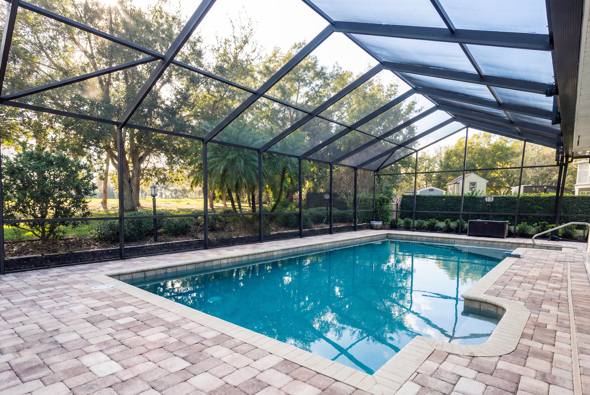 Pool enclosed in a screen with a brick patio, trees and sky visible in the background.
