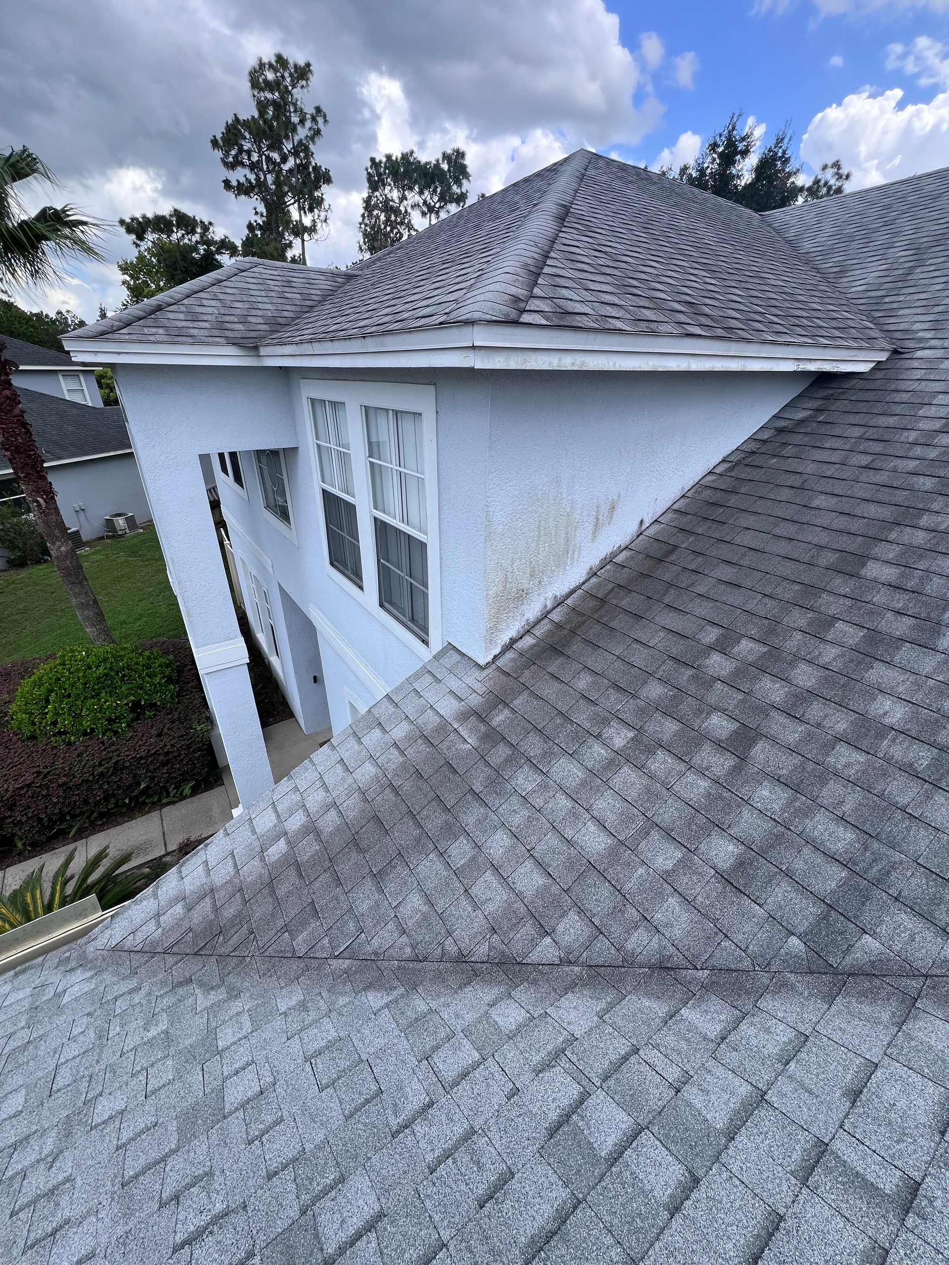 The roof of a white house with a gray shingle roof.