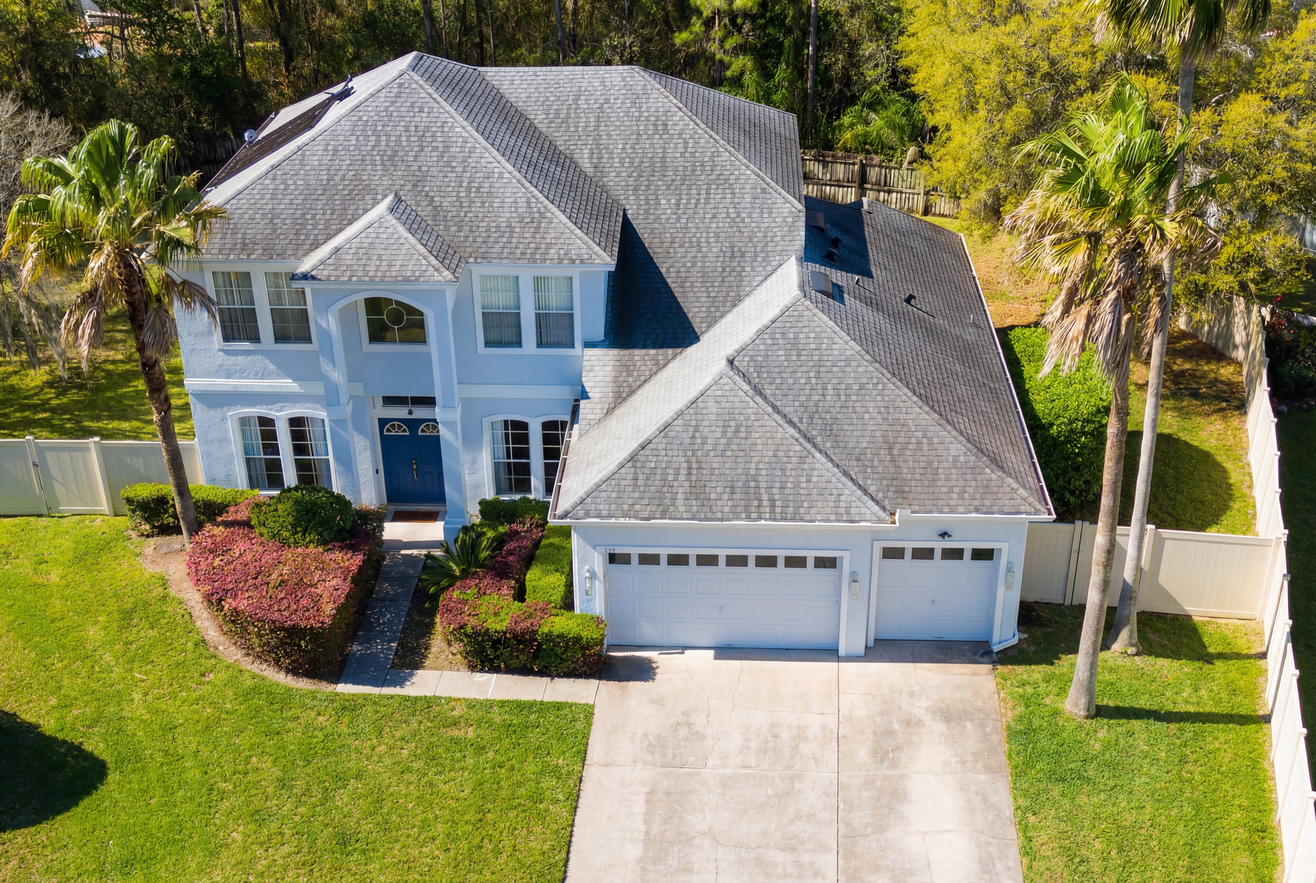 A white house with two garage doors and a palm tree in front of it