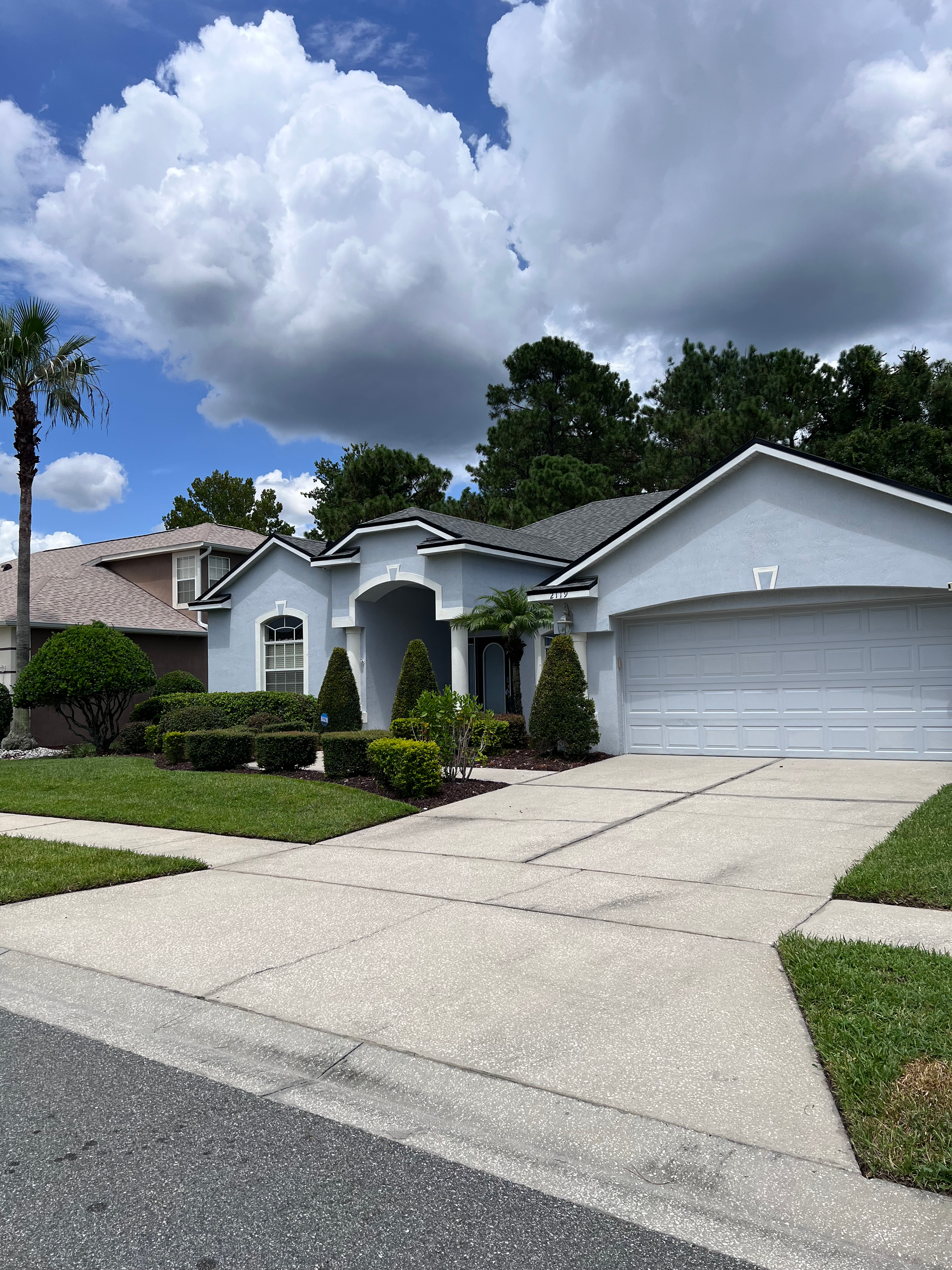 A white house with two garage doors and a palm tree in front of it