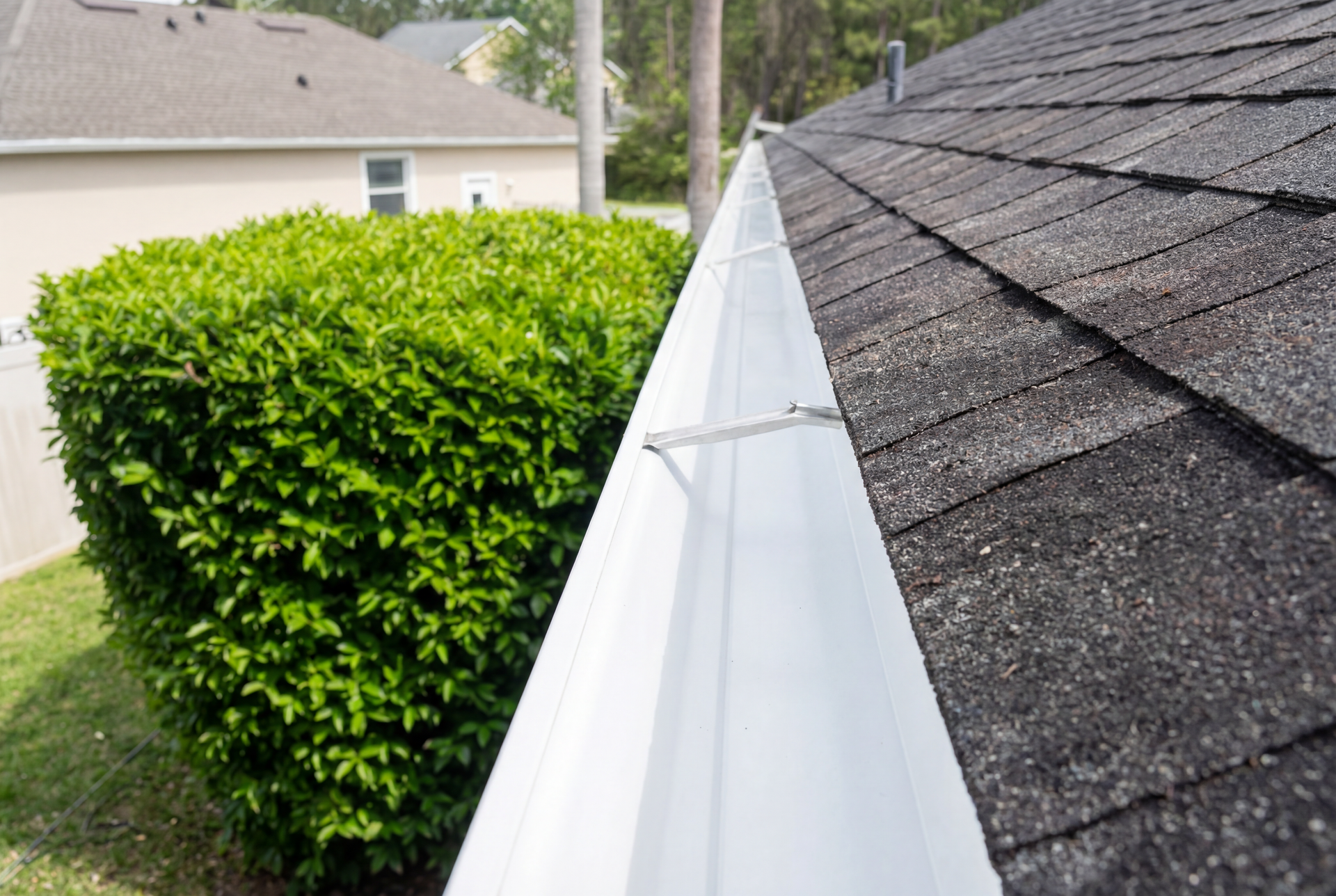 A gutter is sitting on top of a roof next to a bush.