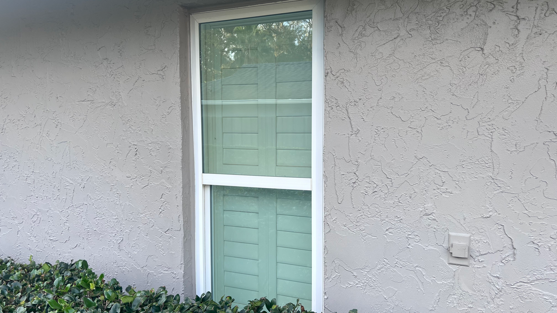 A window on the side of a house with shutters on it.