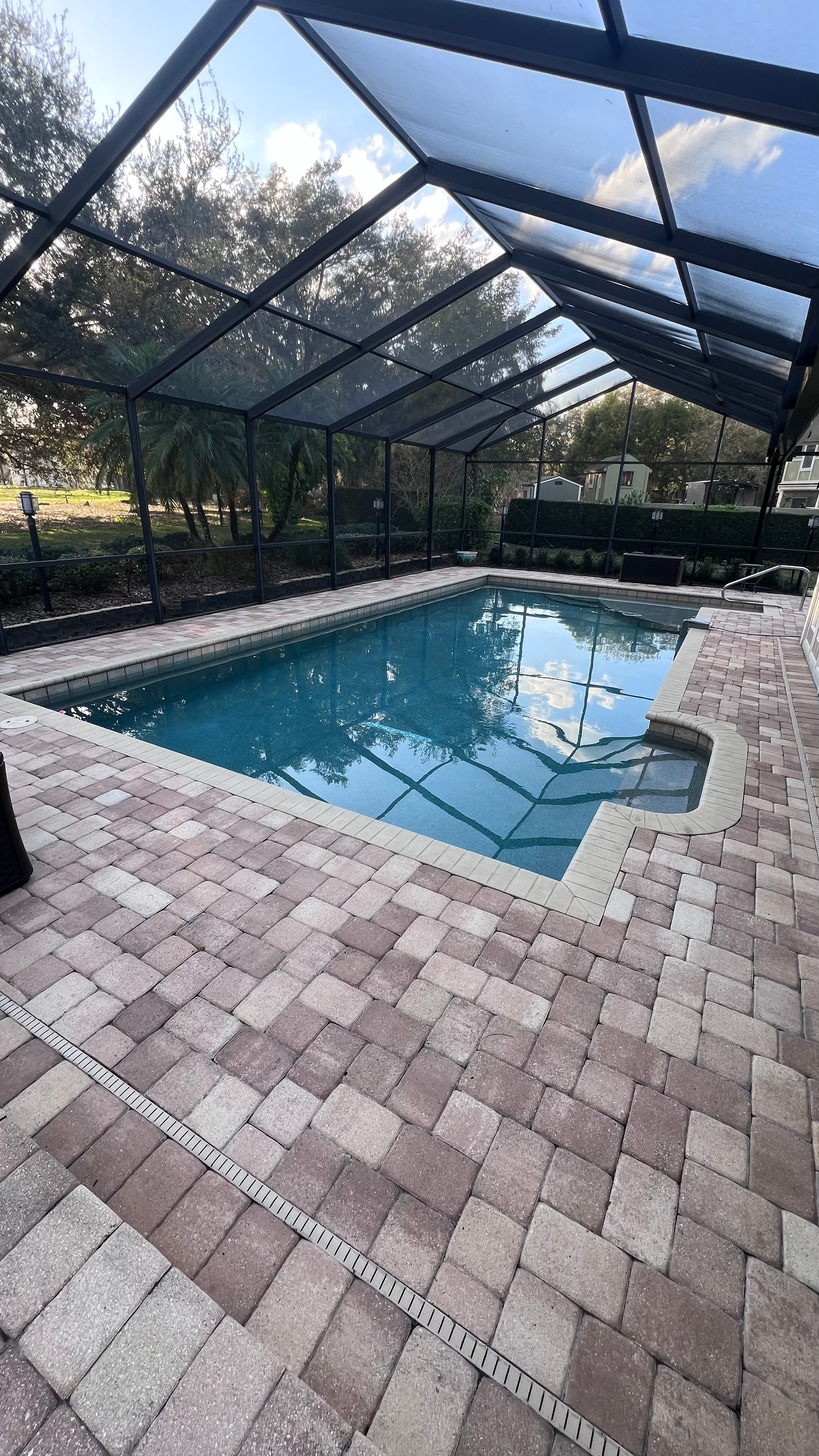 A large swimming pool surrounded by bricks and a screened in area.