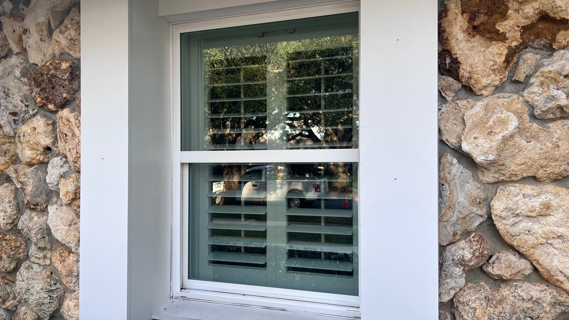 A window with shutters on it is in front of a stone wall.