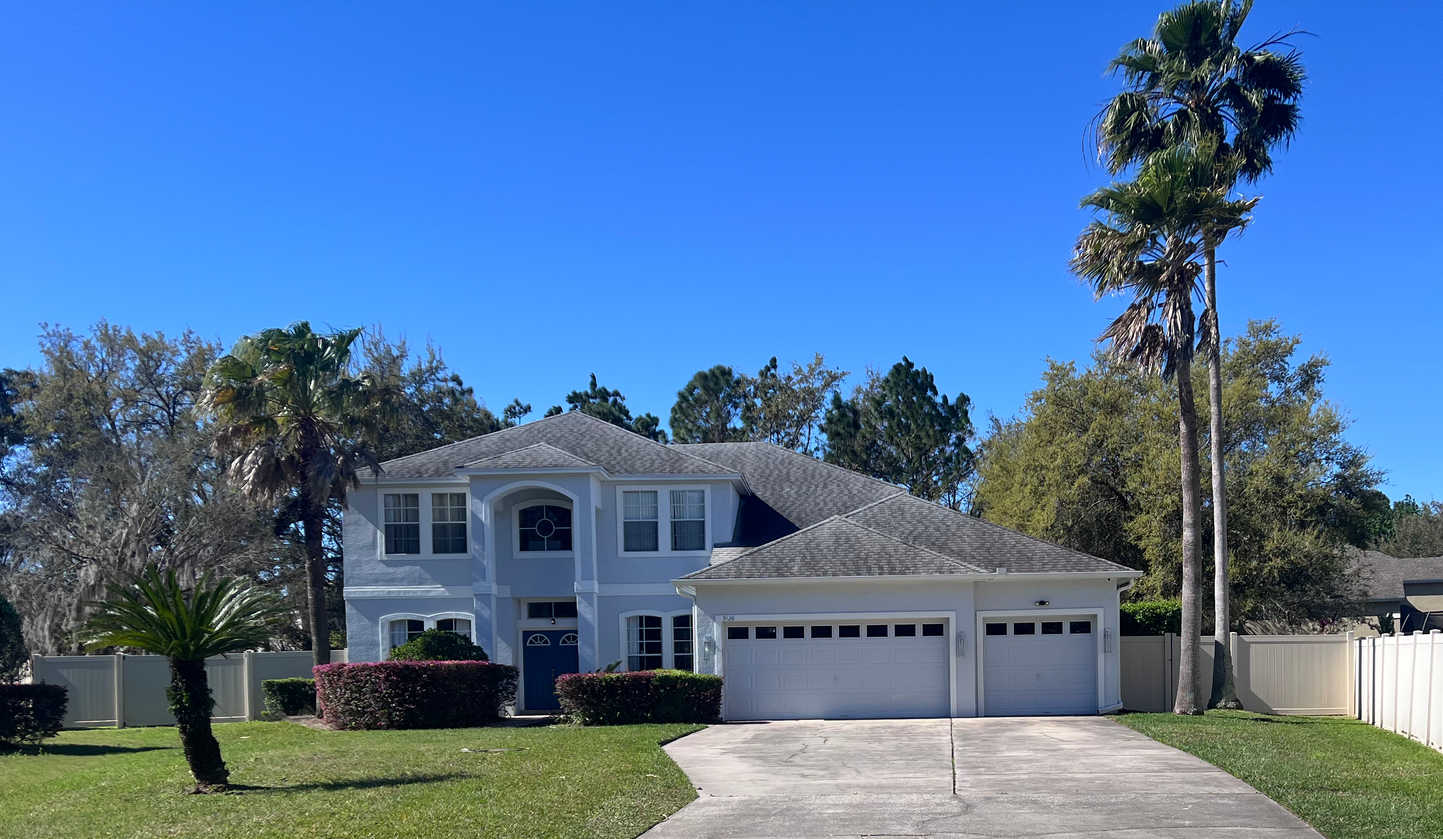 A large white house with a driveway and palm trees in front of it.