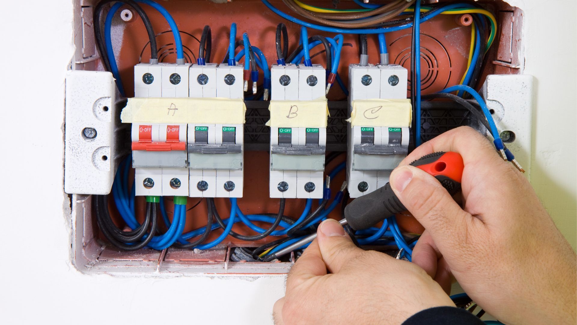 A person is working on an electrical box with a screwdriver.