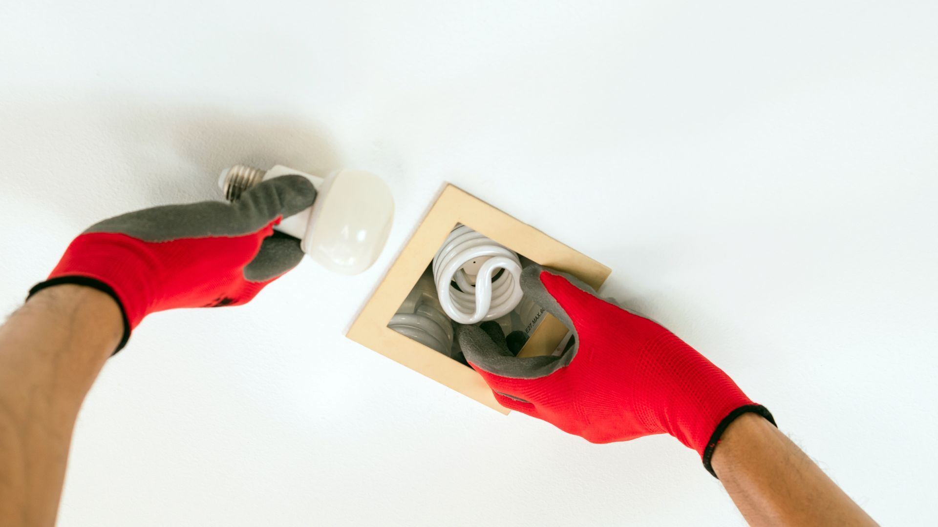 A person wearing red gloves is changing a light bulb.