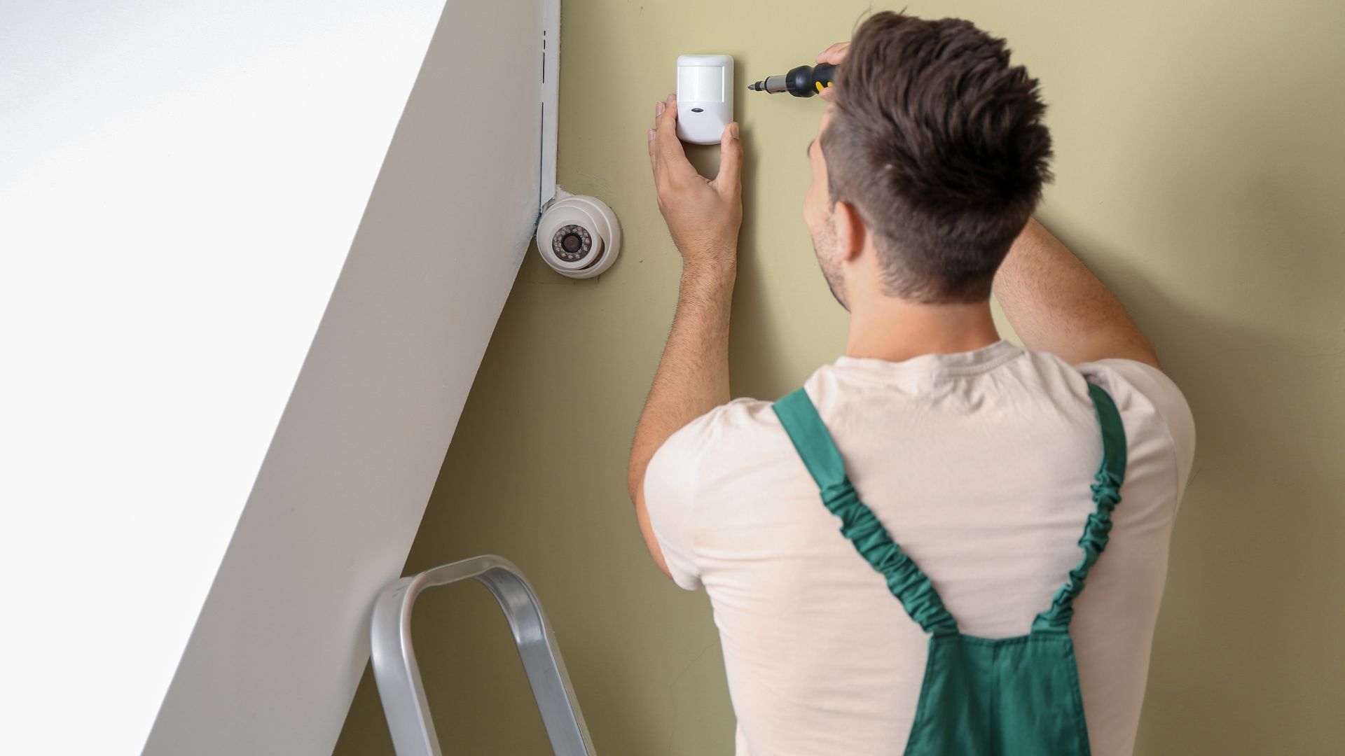 A man is installing a security system on a wall.