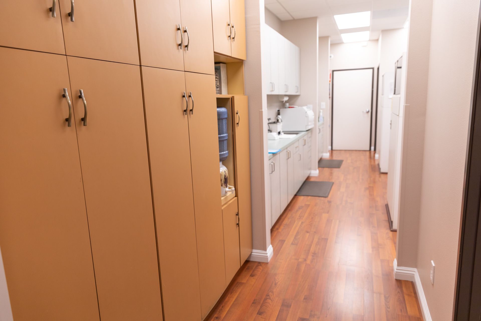 A long hallway with wooden floors and cabinets leading to a kitchen.