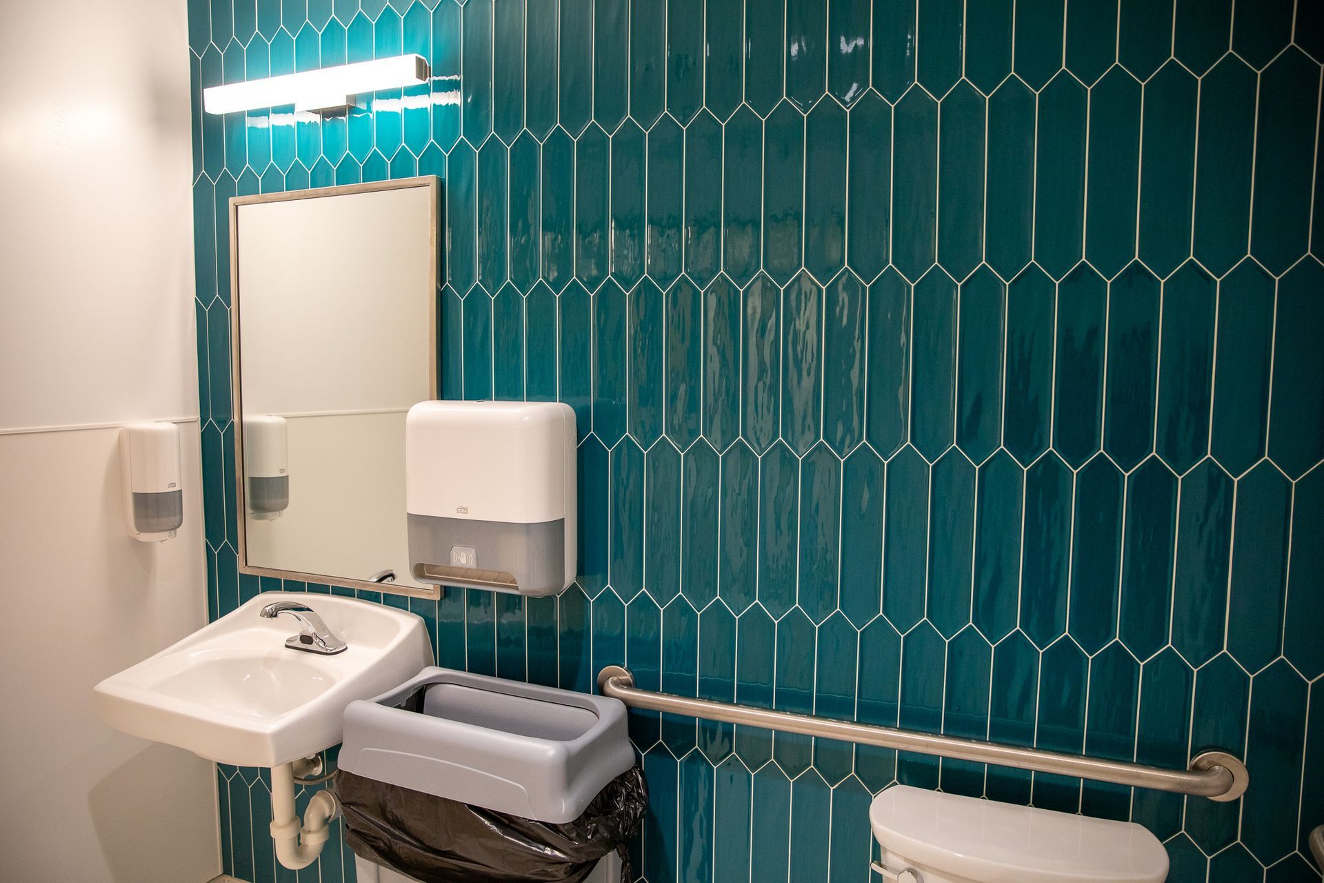A bathroom with a sink , toilet , mirror and trash can.