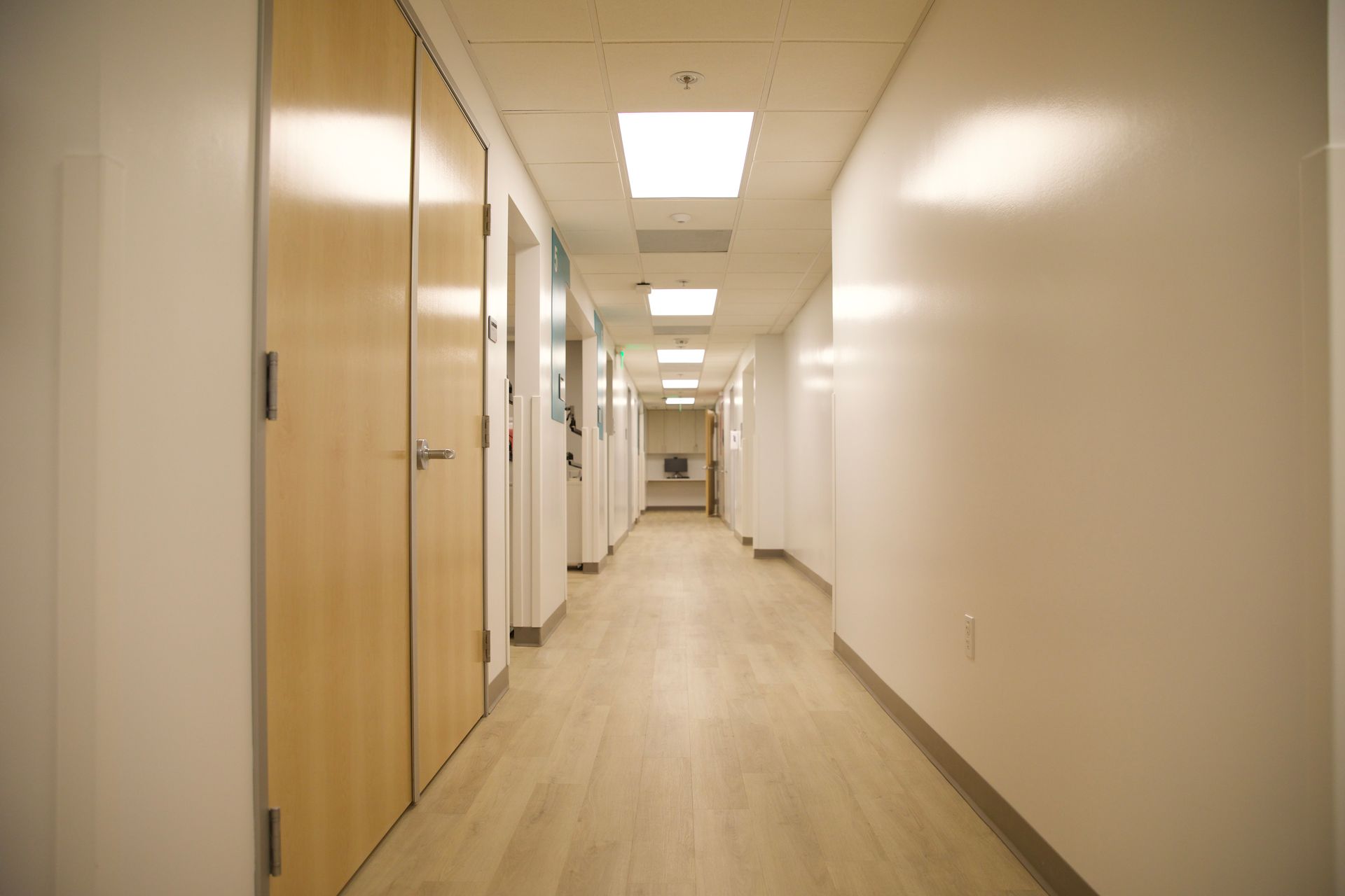An empty hospital hallway with wooden doors and white walls.