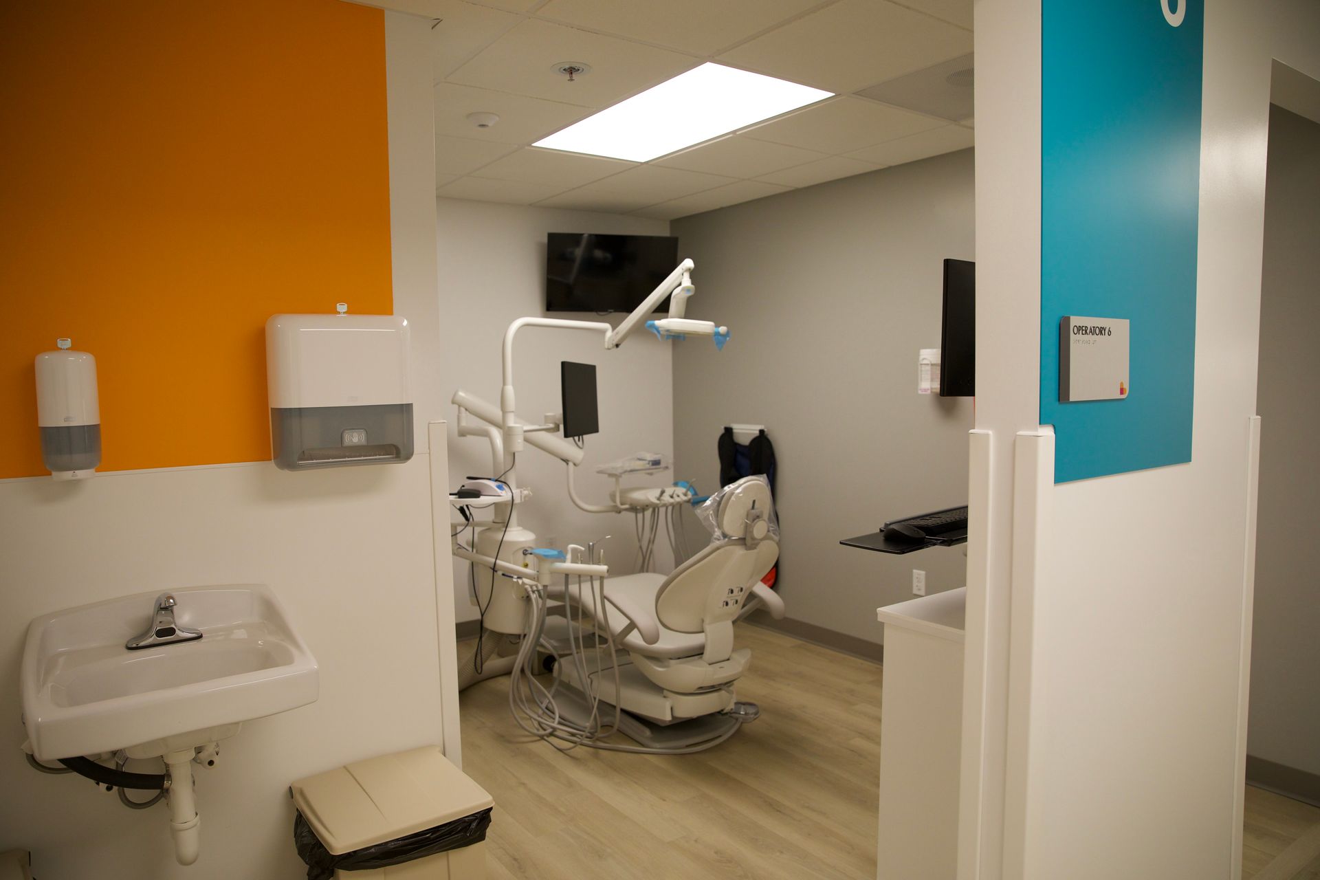 A dental office with a dental chair , sink and television.