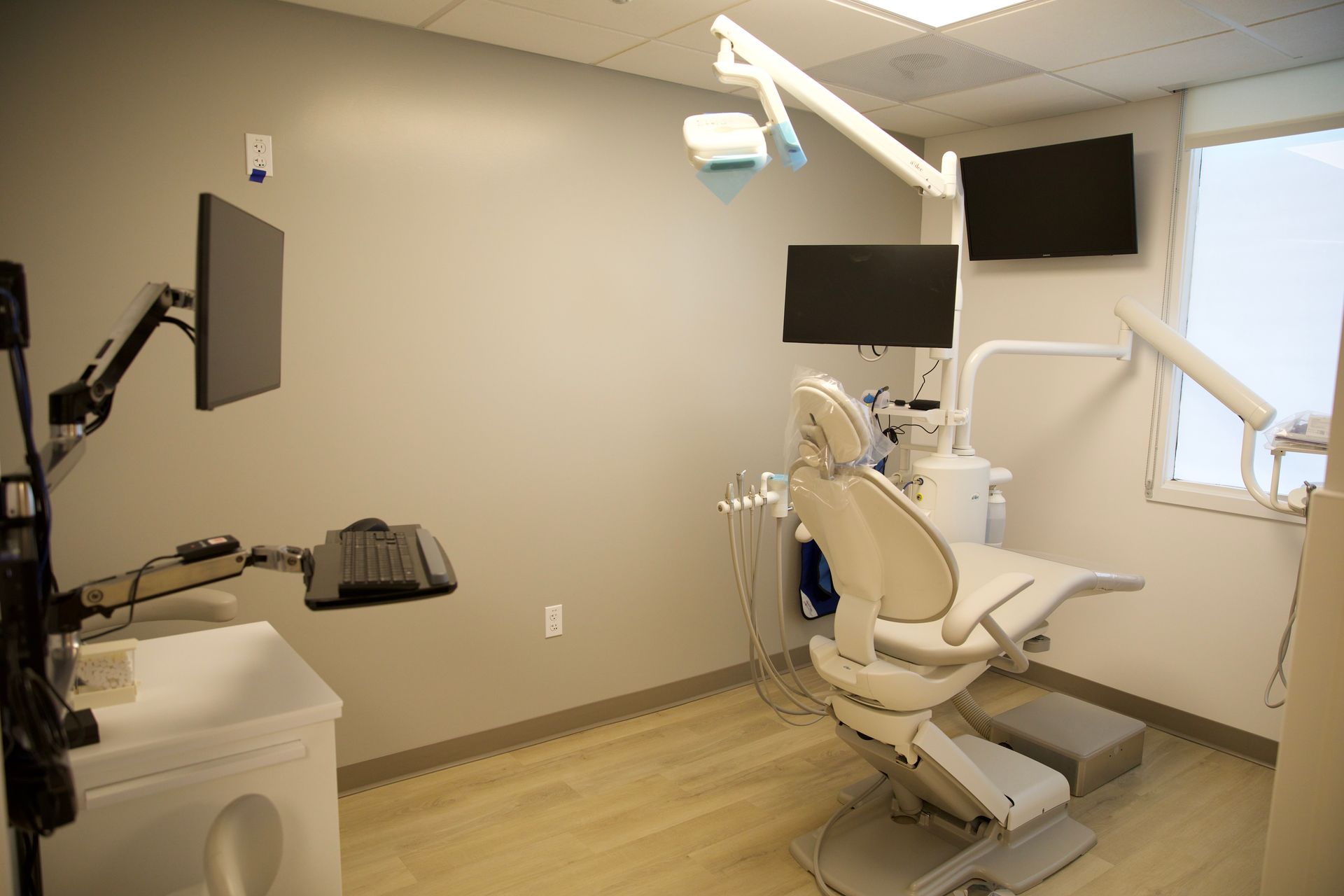 A dental office with a dental chair , monitors , and a sink.