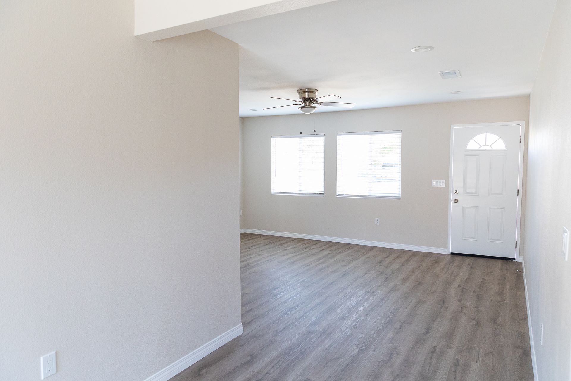 An empty living room with hardwood floors and a ceiling fan.