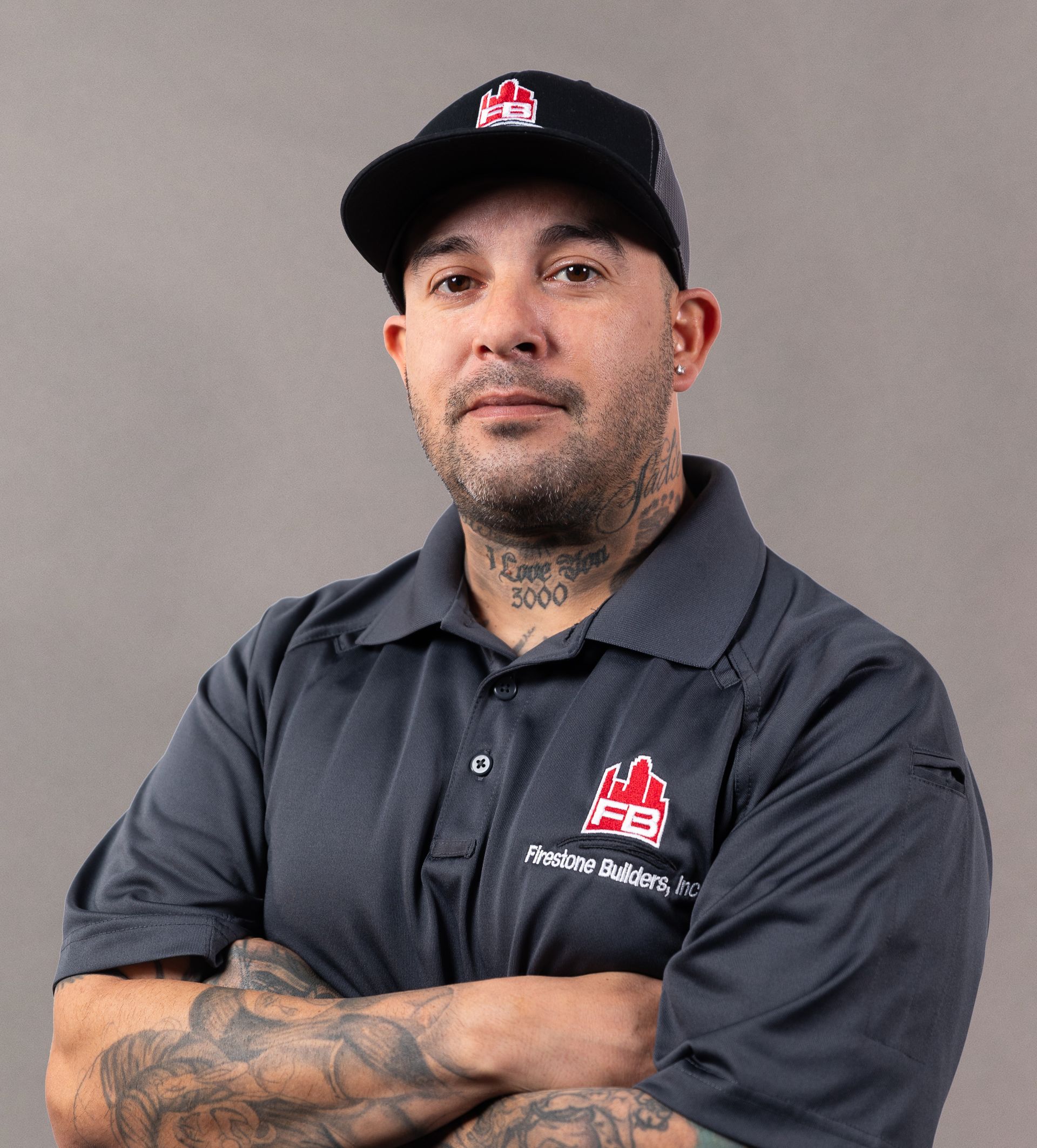 A man with tattoos and a hat is standing with his arms crossed.