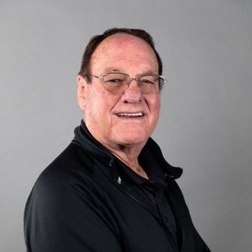 A man wearing glasses and a black jacket is smiling for the camera.